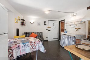A compact room with a bed, a table, a kitchen area with a sink and stove, and a door leading to another room. - Apartment "Bilocale Victor" near the beach (Bonassola SP)