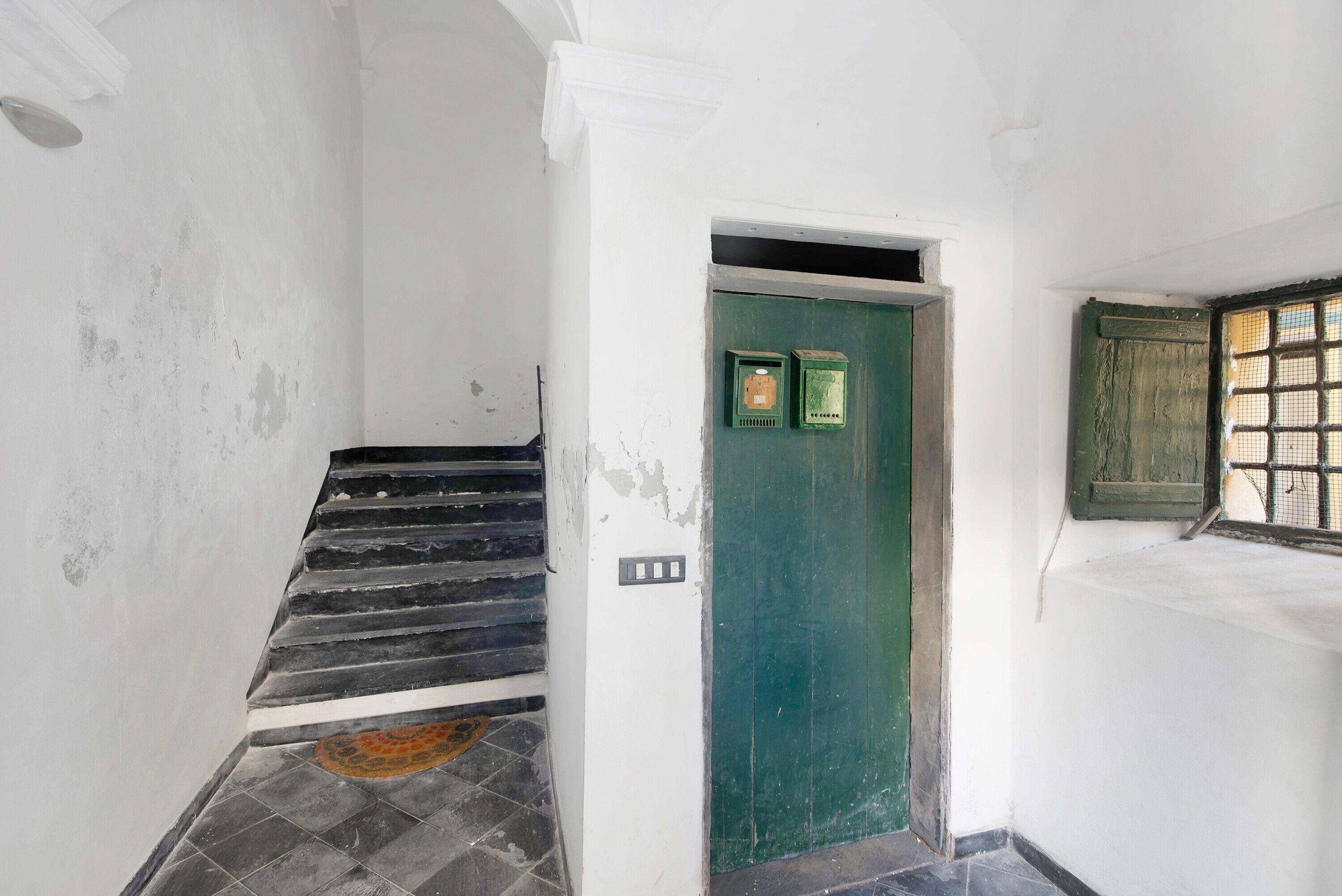 Eine Treppe führt zu einer grünen Tür, an der Wand befinden sich zwei Stromverteilerkästen.