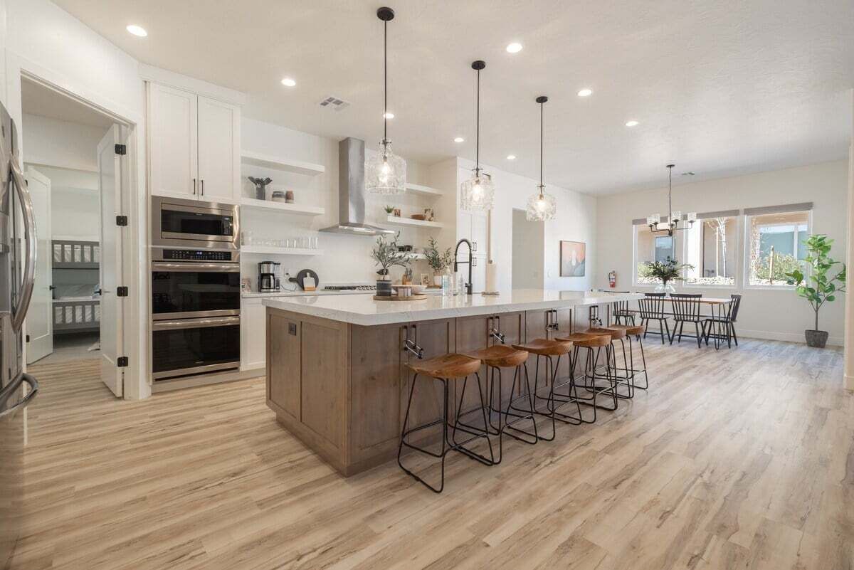 Una cocina moderna con gabinetes blancos, electrodomésticos de acero inoxidable y una isla central con taburetes de bar.
