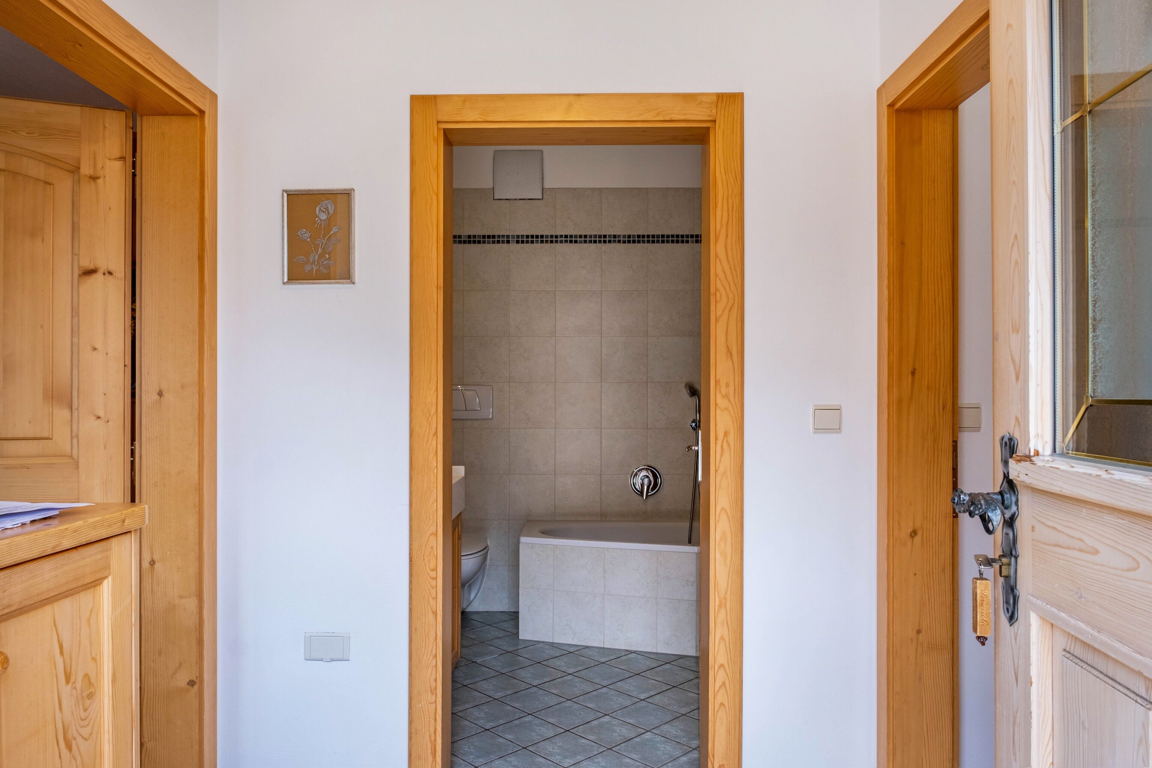 A narrow hallway leading to a bathroom with a bathtub, toilet, and shower.
