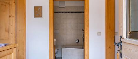 A narrow hallway leading to a bathroom with a bathtub, toilet, and shower.
