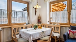A dining area with a table set for two, wooden chairs, a chandelier, and a view of the outside through large windows. - Apartment 'Adlerhorst Zaunkoenig' with Private Terrace and Wi-Fi (Santa Valburga)