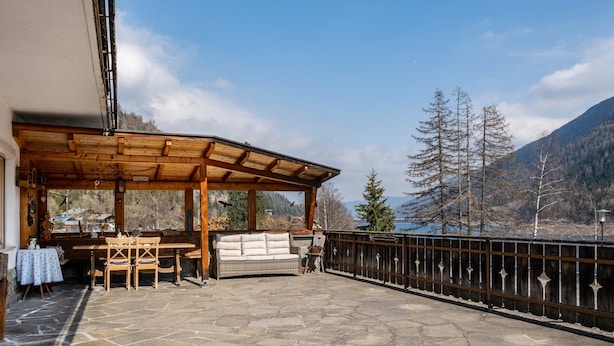 A covered outdoor seating area with stone flooring, wooden furniture, and a view of mountains and a lake. - Apartment 'Adlerhorst Zaunkoenig' with Private Terrace and Wi-Fi (Santa Valburga)