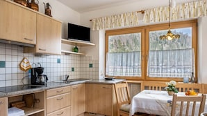 A kitchen with wooden cabinets, a coffee maker, a TV, and a window with a view of trees. - Apartment 'Adlerhorst Zaunkoenig' with Private Terrace and Wi-Fi (Santa Valburga)