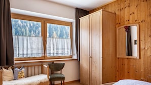 A bedroom with a wooden wardrobe, a chair, a bed, and a window with a view of trees. - Apartment 'Adlerhorst Zaunkoenig' with Private Terrace and Wi-Fi (Santa Valburga)