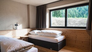 Une chambre avec un lit, une petite table, une lampe et une fenêtre donnant sur des arbres.
