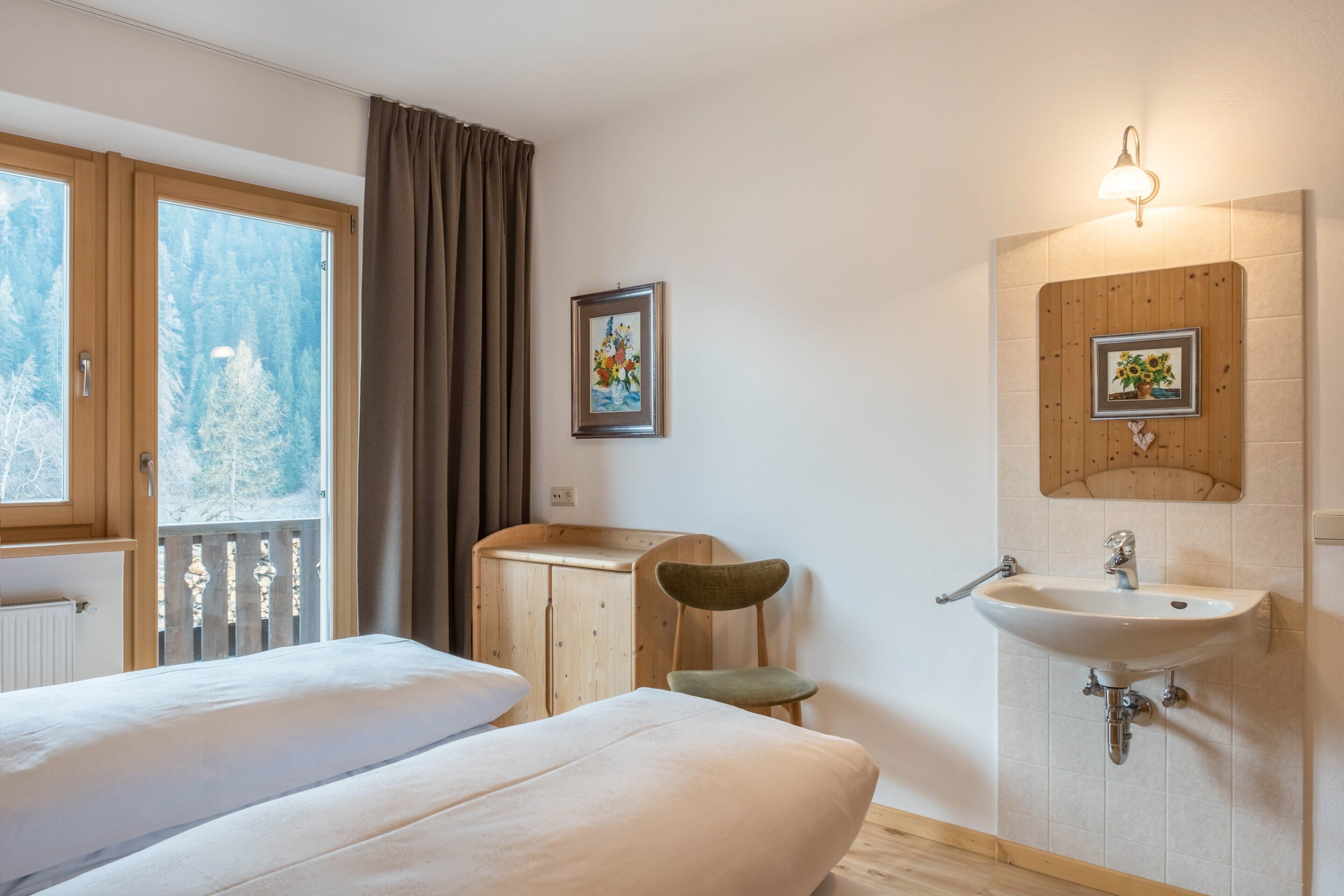 A hotel room with two beds, a wooden cabinet, a chair, a sink, and a window with a view of trees.