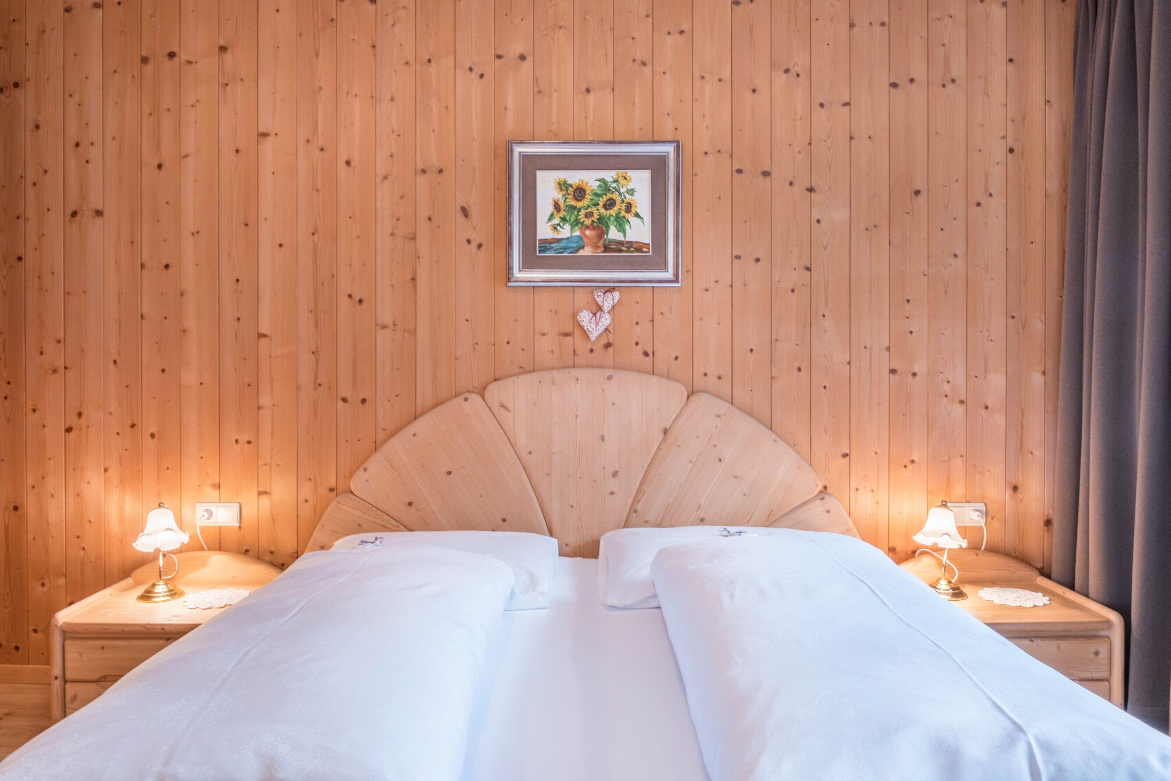 Ein Zimmer mit Holzwänden, einem Bett, zwei Nachttischen mit Lampen, einem gerahmten Bild an der Wand und einer herzförmigen Dekoration.