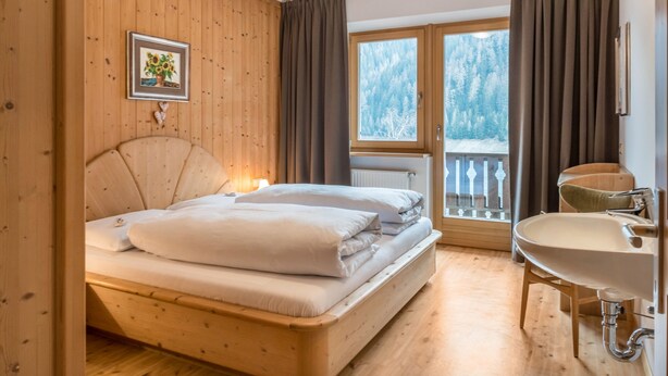 A wooden room with a bed, a window with a view of trees, a bathroom with a sink, and a framed picture on the wall. - Apartment 'Adlerhorst Rotkehlchen' with Balcony, Shared Garden and Wi-Fi (Santa Valburga)