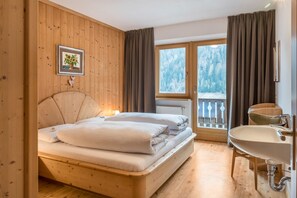 Una habitación de madera con una cama, una ventana con vistas a árboles, un baño con lavabo y un cuadro en la pared.