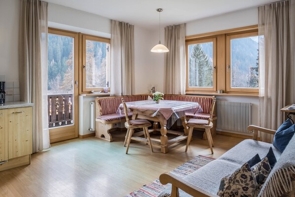 Una habitación acogedora con una mesa de comedor, sillas, un sofá y ventanas amplias con cortinas.