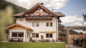 A two-story house with a balcony adorned with flowers, a wooden deck, and a view of a forested mountain. - Apartment 'Adlerhorst Rotkehlchen' with Balcony, Shared Garden and Wi-Fi (Santa Valburga)