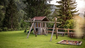 A wooden playhouse with a slide and swing set in a grassy yard with trees and a mountain in the background. - Apartment 'Adlerhorst Blaumeise' with Balcony, Shared Garden and Wi-Fi (Santa Valburga)