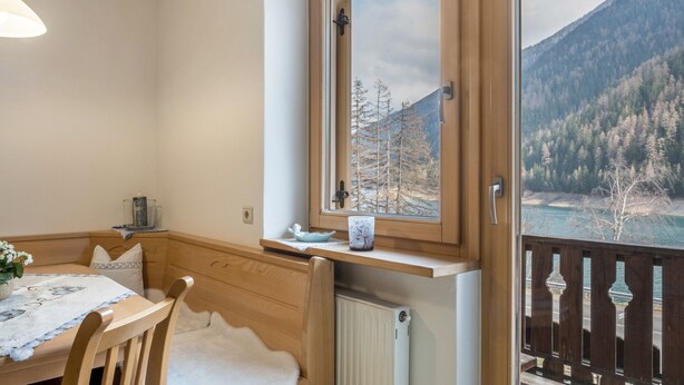 A room with a wooden table, chairs, a window with a view of a forest and mountains, and a balcony with a railing. - Apartment 'Adlerhorst Blaumeise' with Balcony, Shared Garden and Wi-Fi (Santa Valburga)
