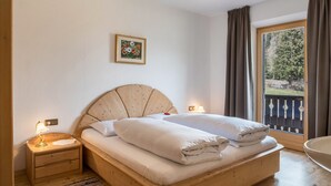 A bedroom with a wooden bed, a nightstand with a lamp, a framed picture on the wall, and a view of a balcony. - Apartment 'Adlerhorst Blaumeise' with Balcony, Shared Garden and Wi-Fi (Santa Valburga)