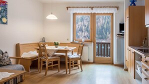 A cozy room with a wooden dining table, chairs, a sofa, a TV, and a window with a view of trees. - Apartment 'Adlerhorst Blaumeise' with Balcony, Shared Garden and Wi-Fi (Santa Valburga)