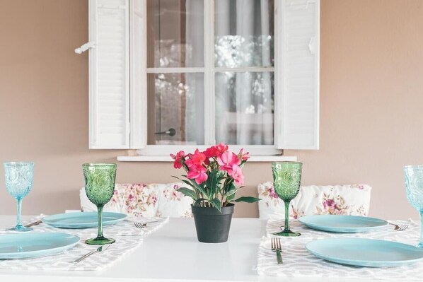 Une table à manger avec des assiettes bleues, de la verrerie verte et une plante en pot ornée de fleurs roses.