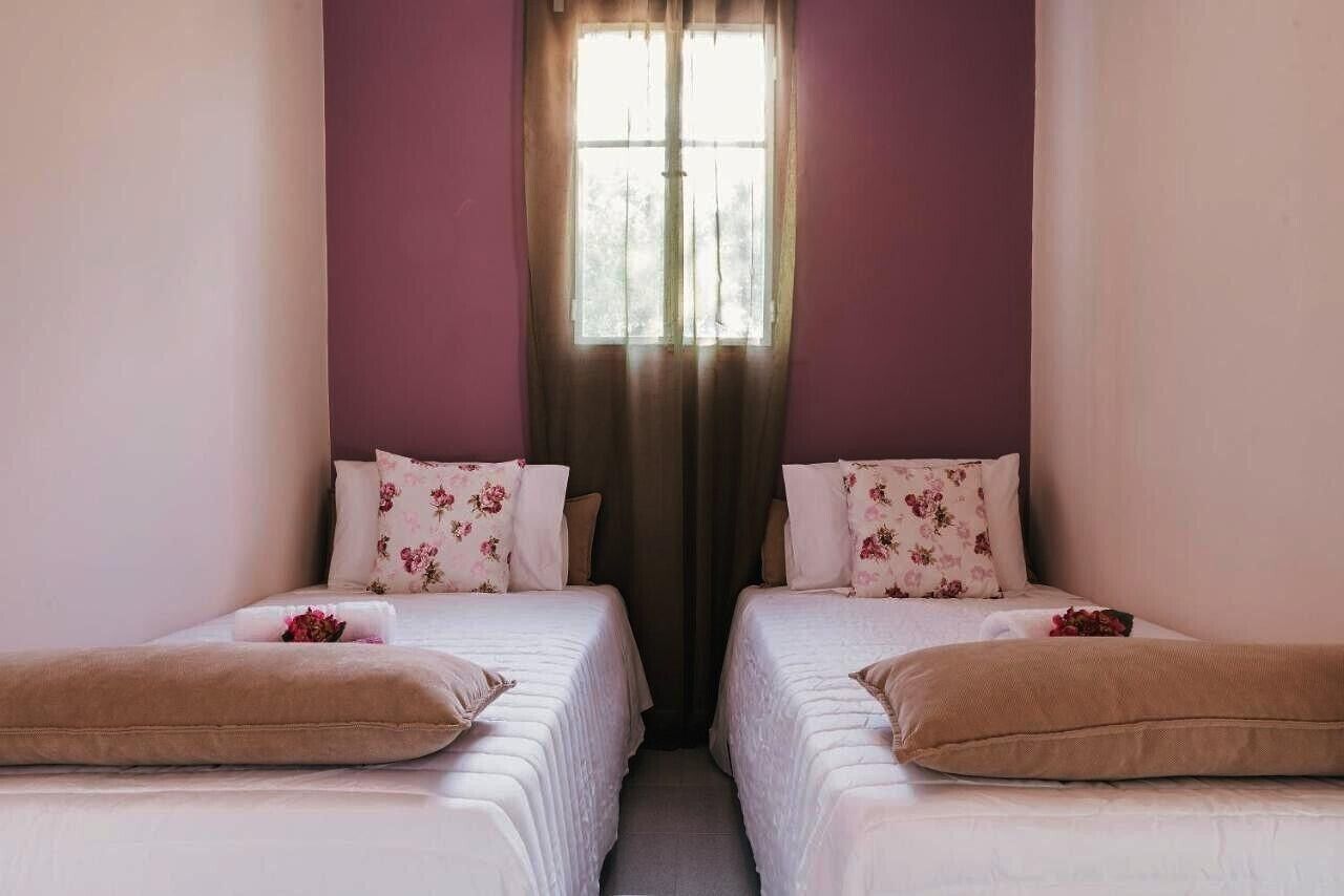 A room with two beds, each with floral pillows and a brown throw blanket.