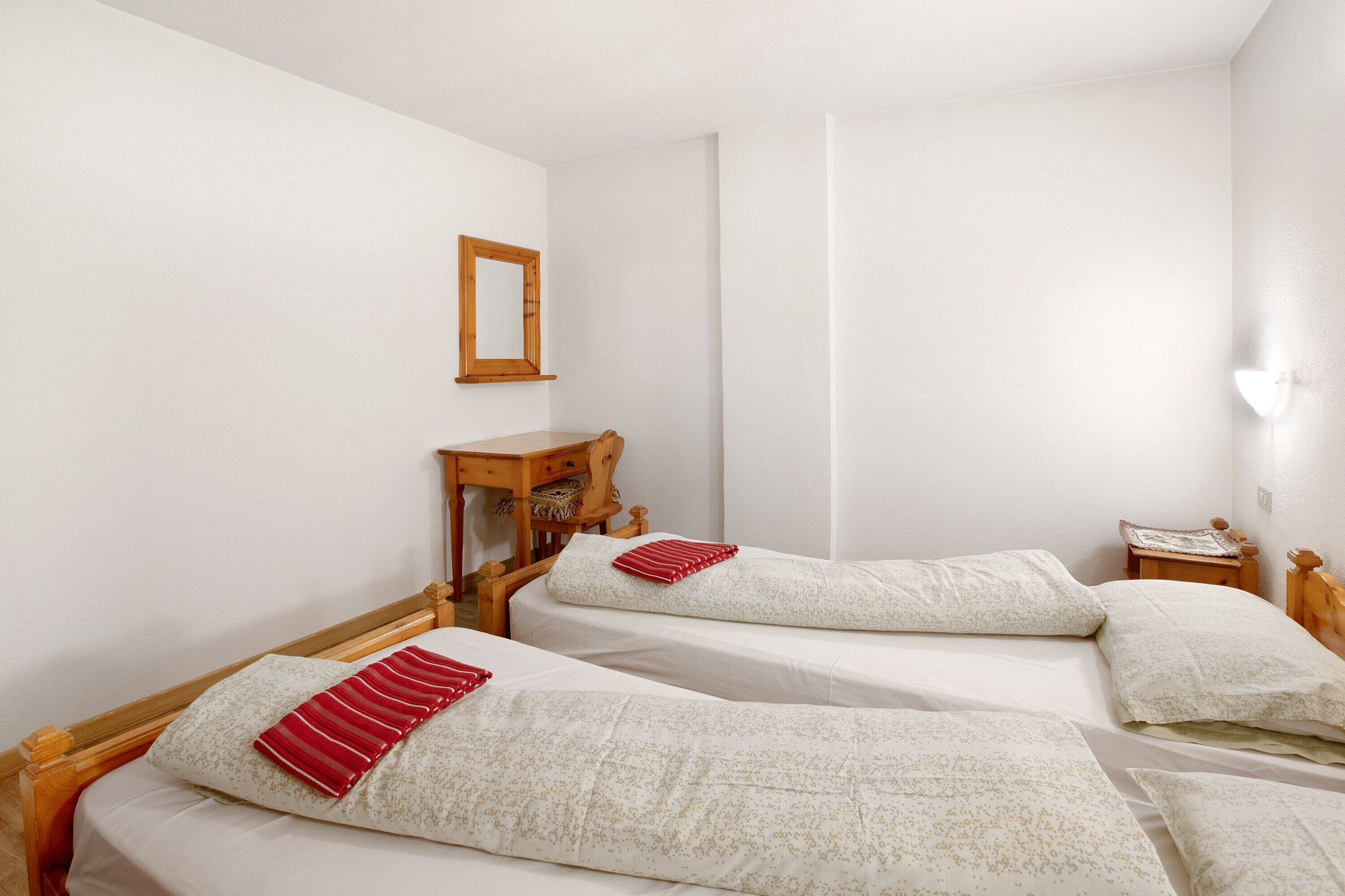 A room with two beds, a wooden nightstand, a mirror, and a wall-mounted light fixture.