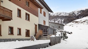 A multi-story building with wooden balconies, a stone wall, and a snow-covered landscape.