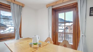 A wooden table with a kettle and cups, a wooden chair, and a view of a snowy landscape through a window.