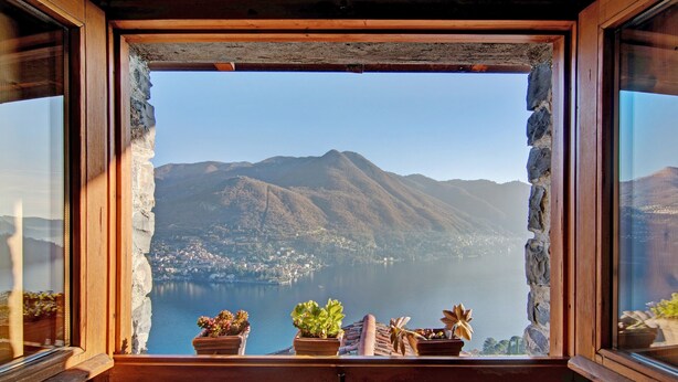 A window with a view of a lake and mountains, wooden window frame, and potted plants on the windowsill. - Holiday Home 'Stone House Of The Year 1500' with Lake View, Private Terrace and Wi-Fi (Moltrasio)