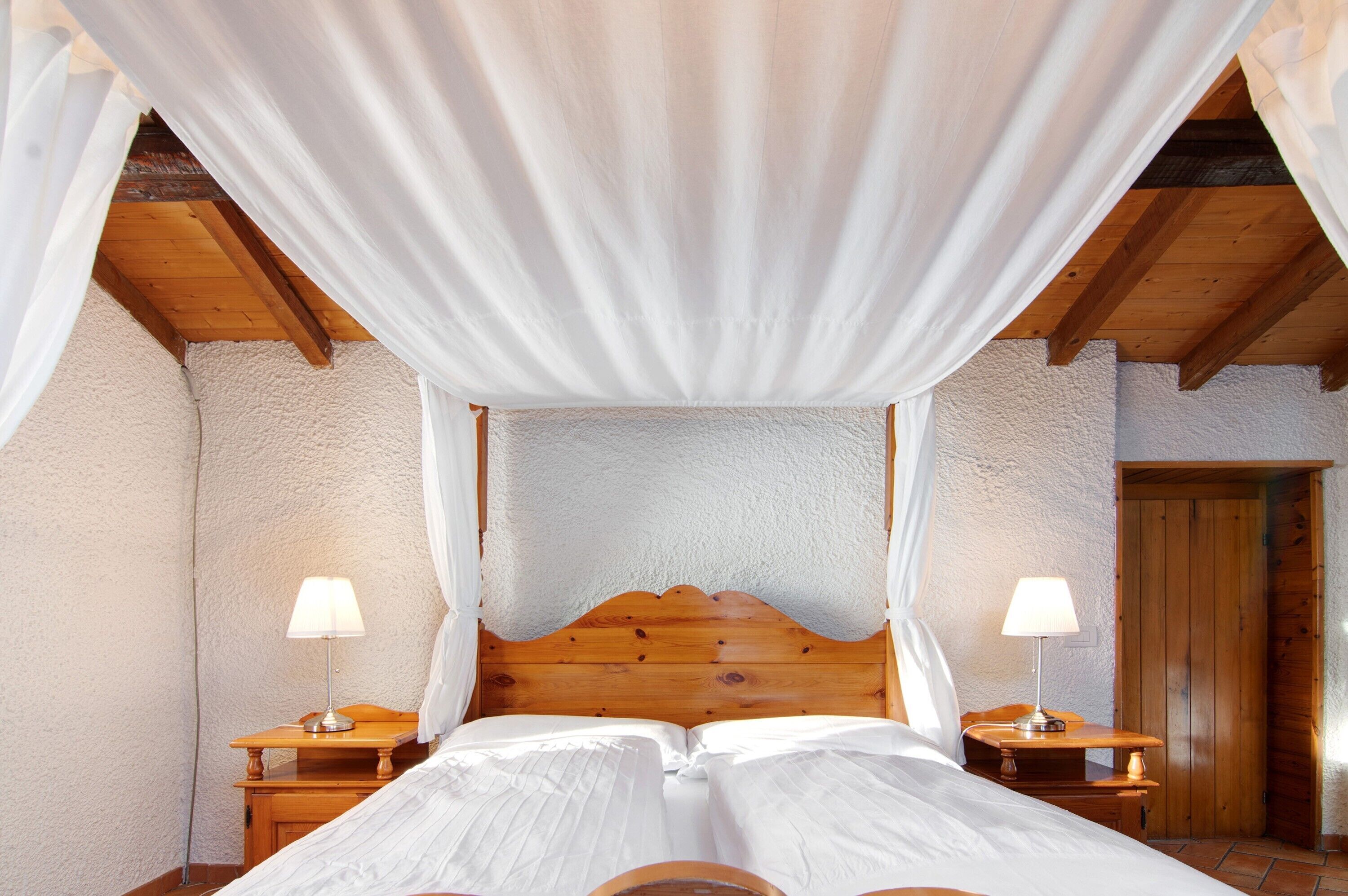 Ein Schlafzimmer mit einem hölzernen Kopfteil, zwei Nachttischen mit Lampen und einem Baldachinbett.