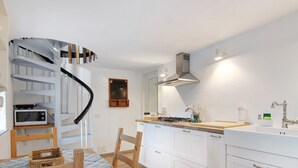 A kitchen with white cabinets, a wooden dining table, a spiral staircase, and a microwave. - Holiday Home 'Stone House Of The Year 1500' with Lake View, Private Terrace and Wi-Fi (Moltrasio)