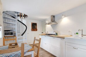 Una cucina con mobili bianchi, un tavolo da pranzo in legno e una scala a chiocciola, oltre a un forno a microonde.