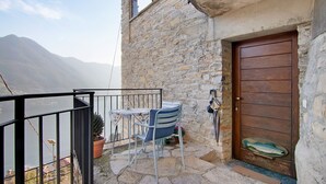 Un edificio de piedra con puerta de madera, un balcón con mesa y sillas, y vista a las montañas.