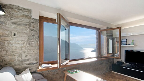 Una sala de estar con pared de piedra, un ventanal con vistas al mar, un sofá, una mesa y un televisor.