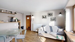 Un espacio de estar moderno con una mesa de vidrio, un sofá y una mesa de centro. Hay estanterías con utensilios de cocina y cuadros en la pared.