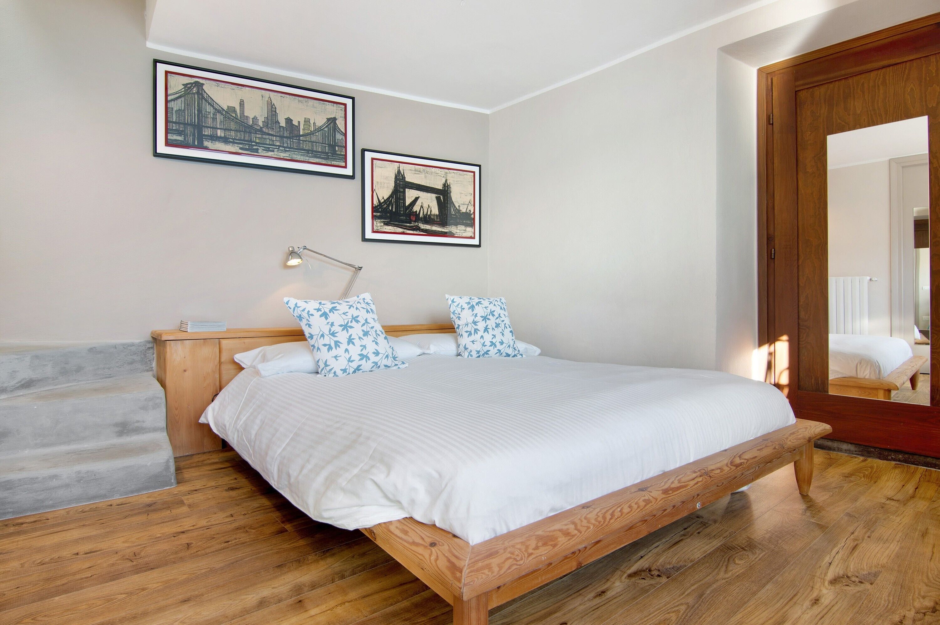 Un dormitorio con una cama de madera, una mesita de noche, una lámpara y dos cuadros en la pared.