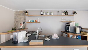 Una cocina compacta con estufa integrada, un lavamanos y una encimera. Hay estantes sobre la encimera con diversos utensilios de cocina y botellas.