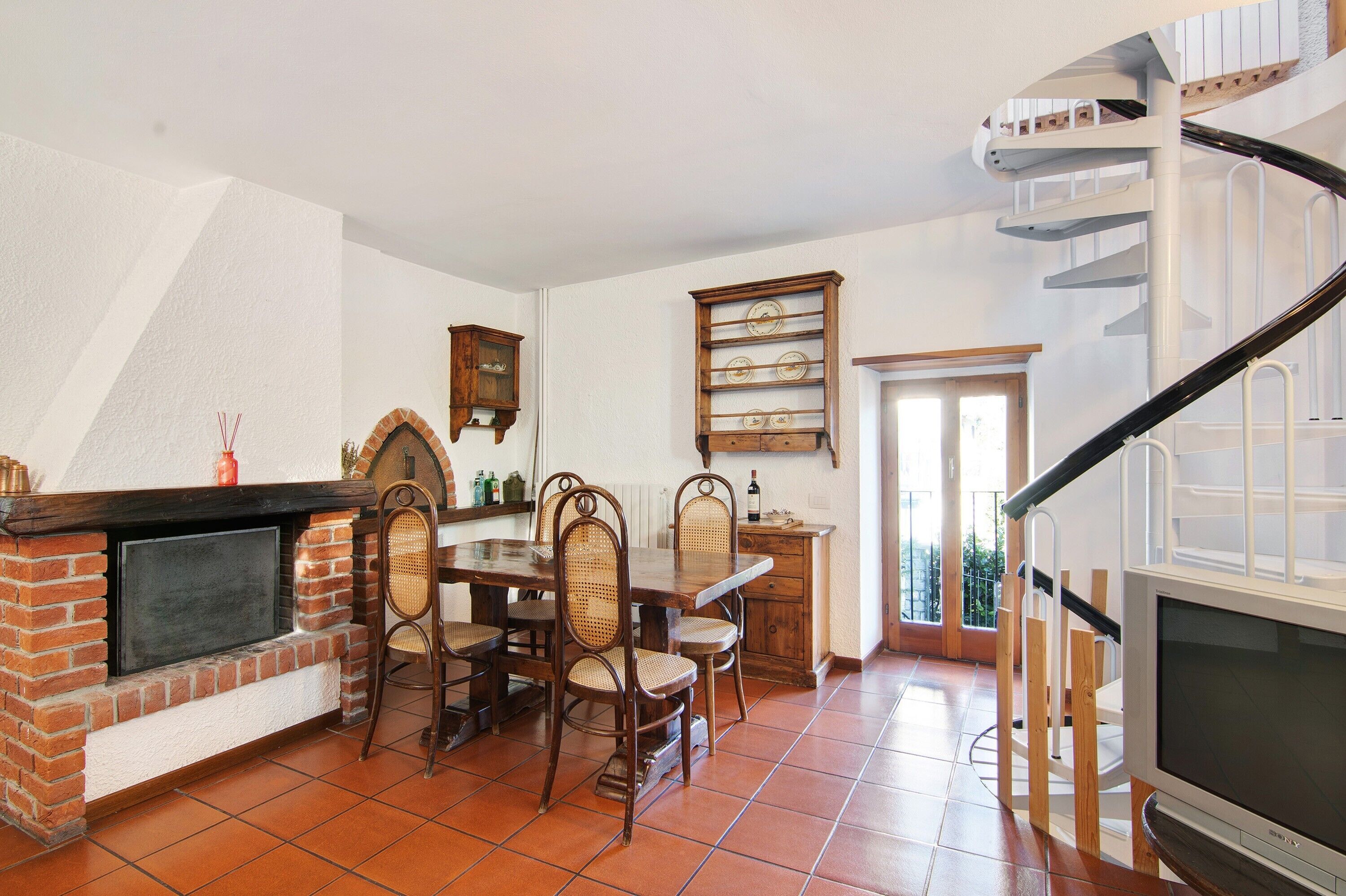 Un comedor con chimenea de ladrillo, sillas de madera, una mesa de comedor y una escalera en espiral.
