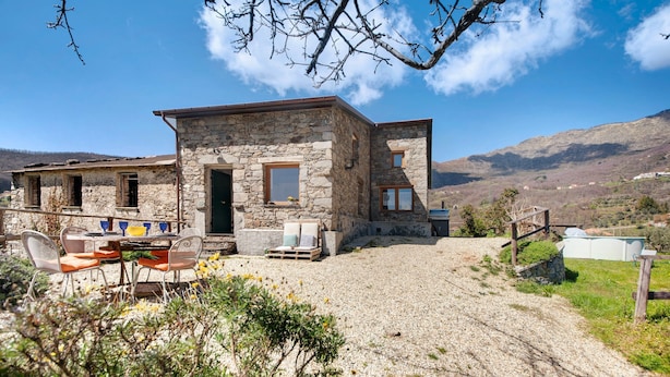 Un bâtiment en pierre avec une allée gravillonnée, des sièges à l’extérieur et une vue sur les montagnes.