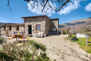 A stone building with a gravel driveway, outdoor seating, and a view of mountains. - Vacation Home "Nature House Custu Giancu" with Mountain View, Pool & Wi-Fi (Costa di Cichero)