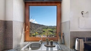 Une cuisine avec une fenêtre donnant sur un paysage, un évier, une machine à café et un cactus posé sur le plan de travail.
