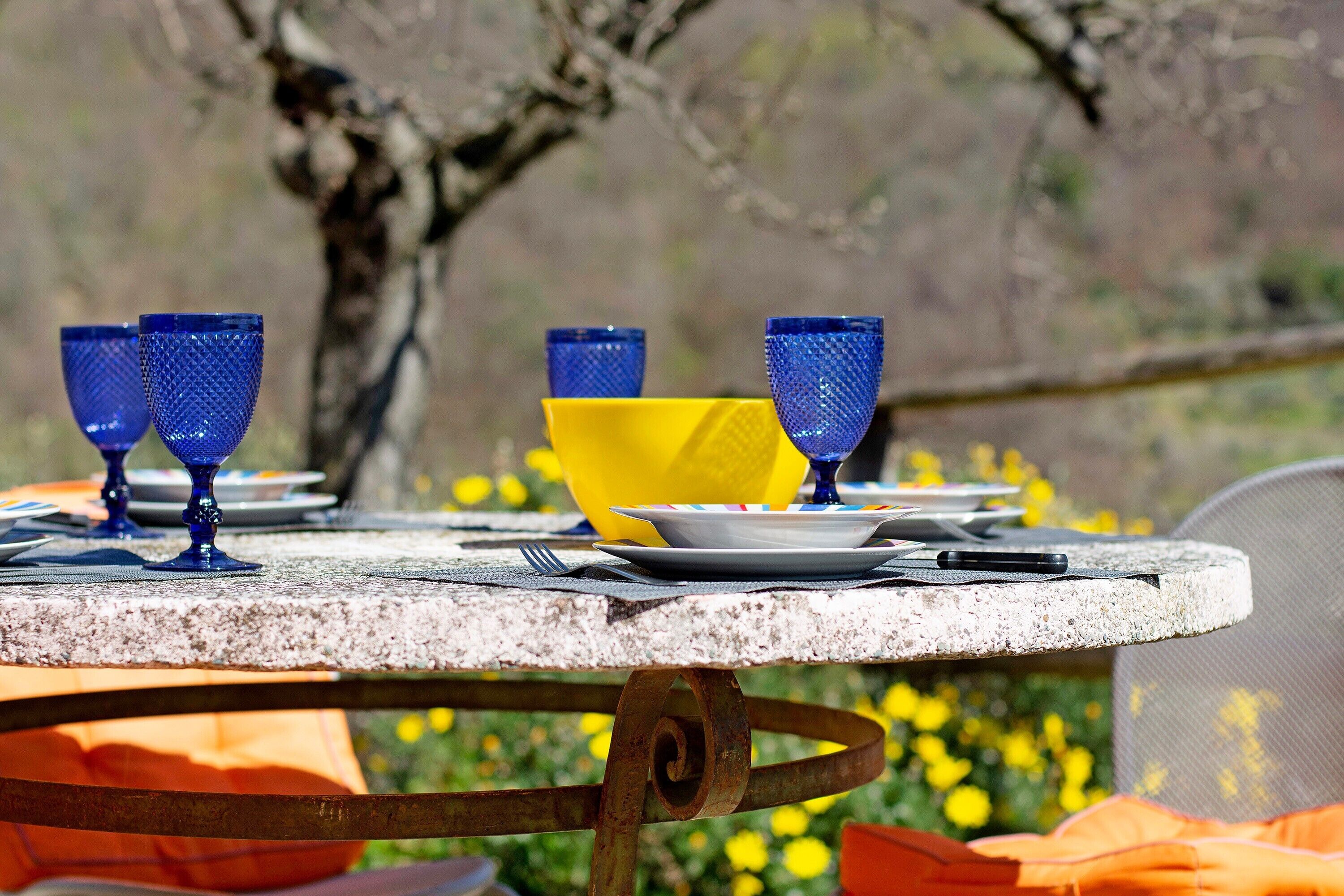 A table set outdoors with blue and yellow glassware, a plate, and a smartphone.