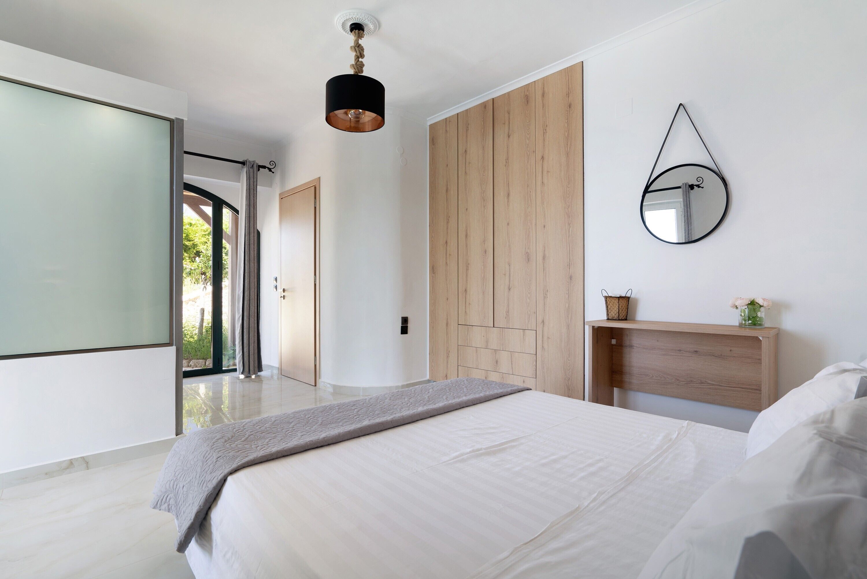 A modern bedroom with a large bed, a wooden wardrobe, a mirror, and a ceiling light.