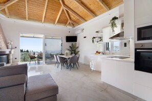 A modern kitchen with a large island, a dining area with a table and chairs, and a view through the glass door.