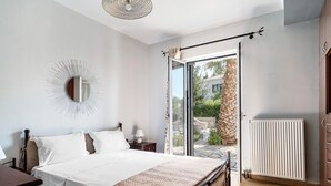 Une chambre à coucher comprenant un lit, une table de chevet, une lampe, un miroir, un radiateur et une porte-fenêtre coulissante donnant sur un espace extérieur.