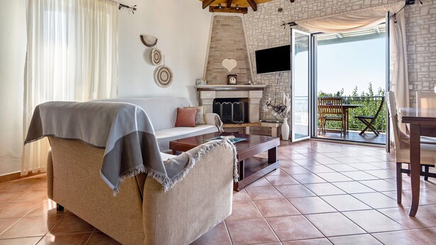 Un salon confortable avec un canapé, une cheminée, un téléviseur et un balcon agrémenté de mobilier d’extérieur.