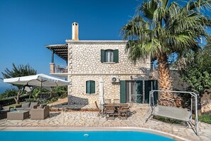 A stone building with a pool, outdoor furniture, and a palm tree.