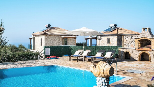 A swimming pool with lounge chairs and umbrellas, a stone building with a tiled roof, and a clear sky. - "Villa Alexandros" with Sea View, Private Pool & Wi-Fi (Lefkada)