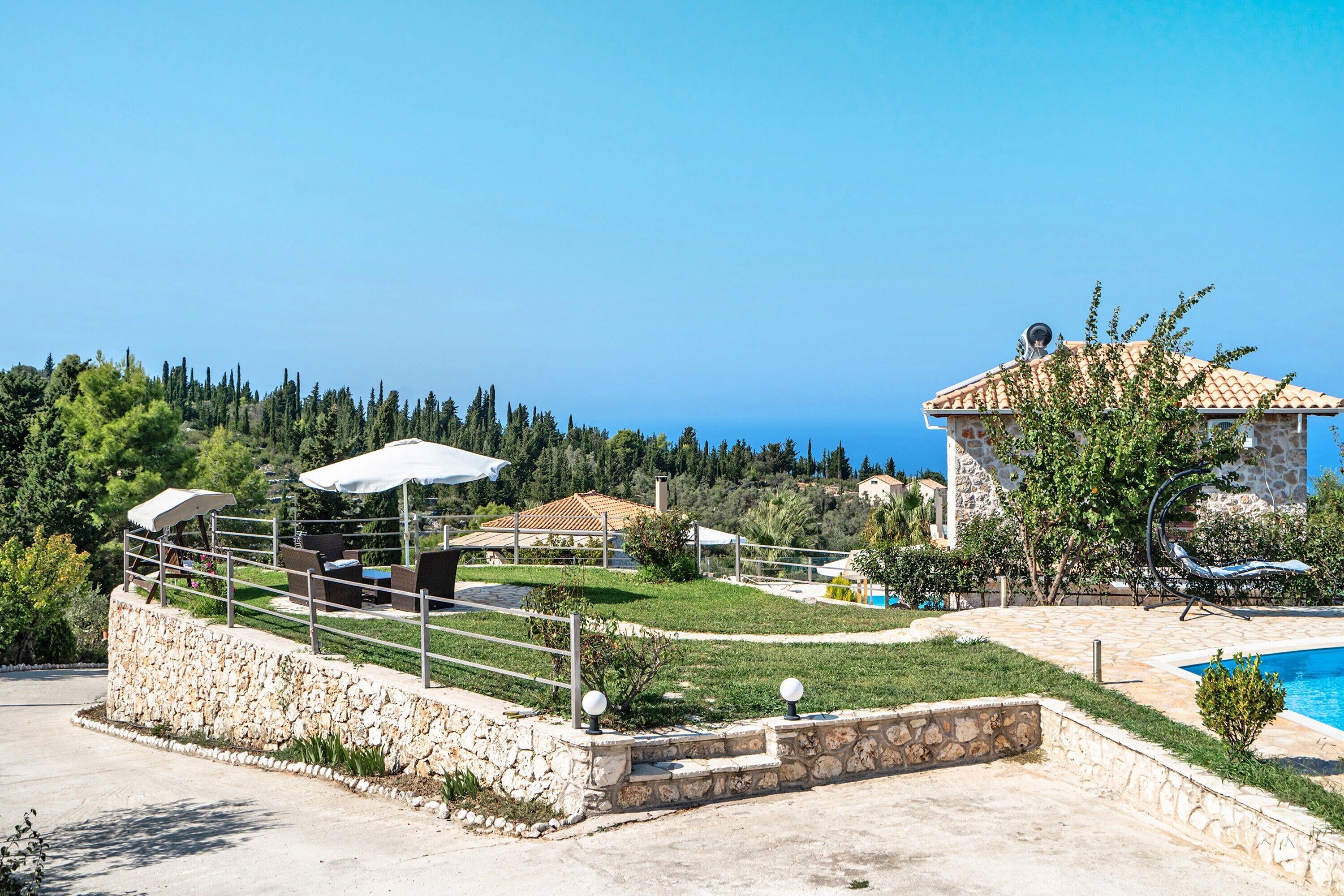 Zona exterior amb parets de pedra, piscina, gandules i vistes al mar.