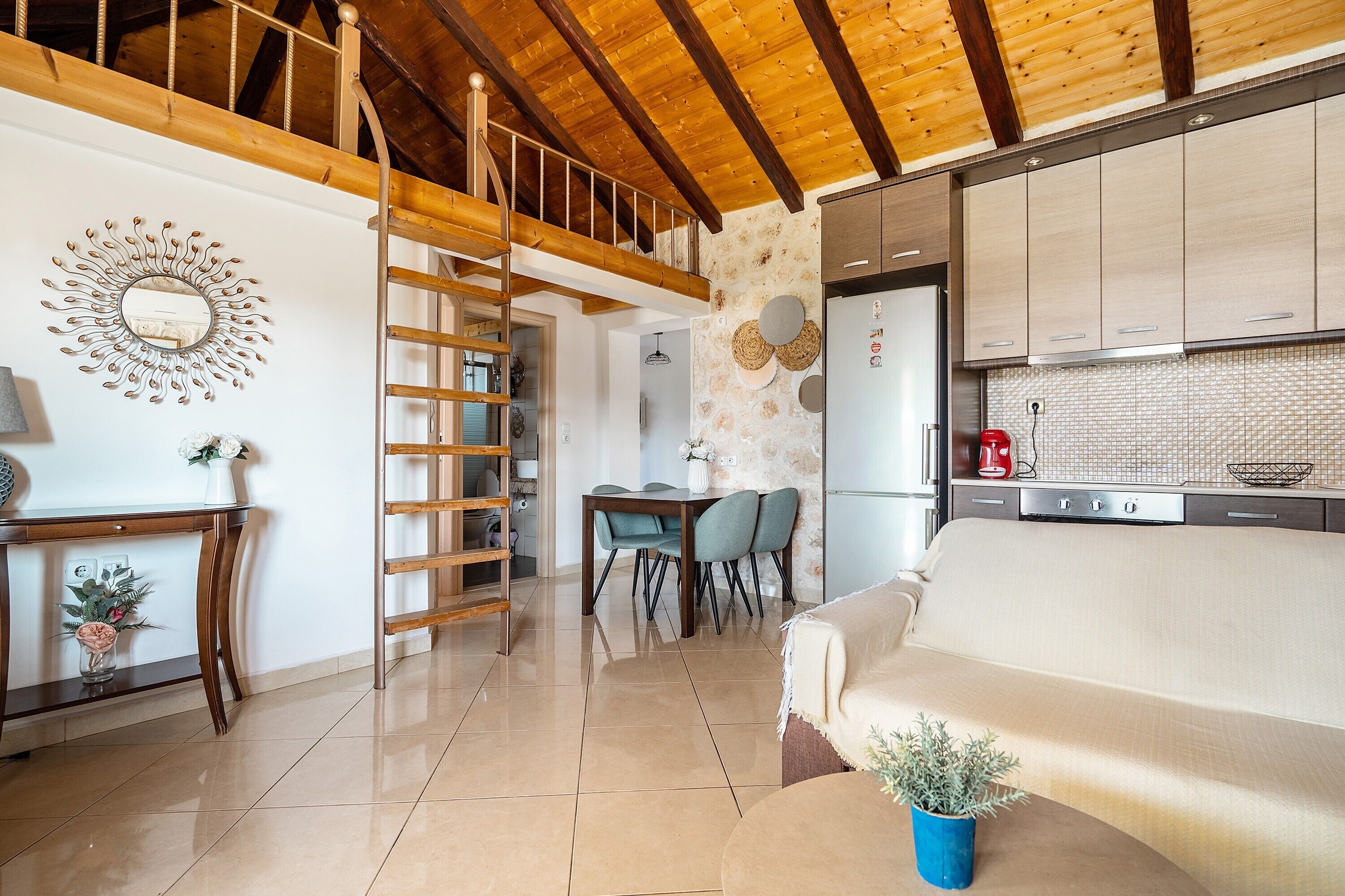 A modern kitchen with a dining area, wooden ceiling beams, and a staircase.