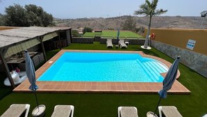 Ein rechteckiger Swimmingpool mit Fliesenrand, umgeben von Kunstrasen und einer Steinmauer.
