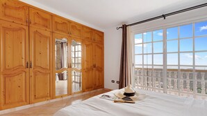 Ein Schlafzimmer mit einem großen Bett, einem Holzschrank und einem Balkon mit Blick.