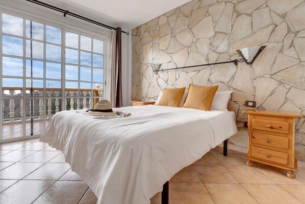 Une chambre avec un grand lit, un mur en pierre, une table de chevet et une vue par la fenêtre.